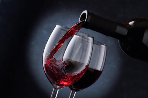 Red wine is poured into a glass from a bottle on a blurry blue background, a stream of red wine from the bottle swirls in the glass, close-up.